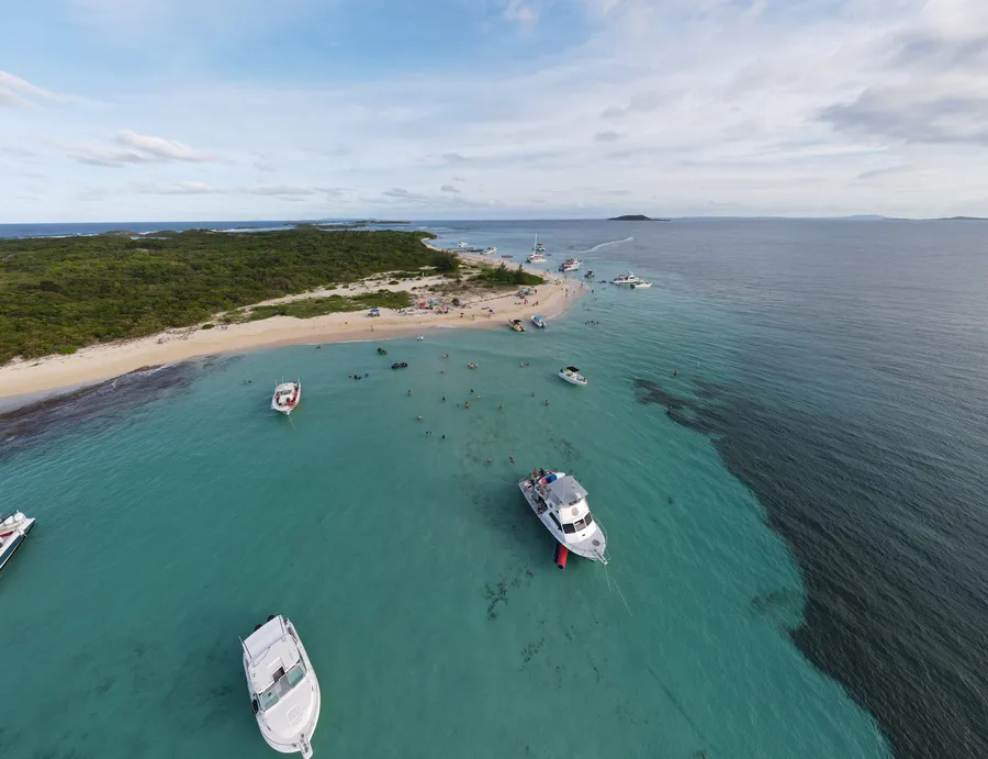 Vista aérea de Cayo Icacos: la playa de arena, bañistas en el agua baja y varios botes fondeados frente a la costa