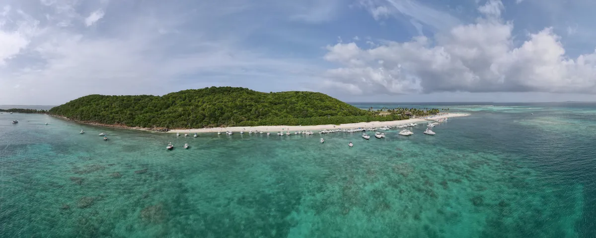 Vista aérea panorámica de una isla con playa de arena y botes fondeados a lo largo de la orilla